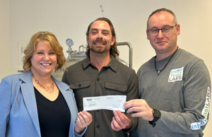Nicole Shoaf, Kyle Adams, and Chris Eskiw standing together holding a cheque 